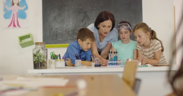 Escola Primária de Ciência Sala de aula: Professor Entusiástico Explica Química para Grupo Diverso de Crianças, Menino Mistura Produtos Químicos em Beakers. Crianças aprendem com interesse — Vídeo de Stock