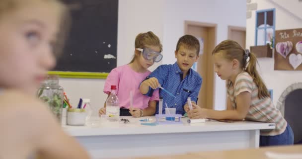Szkoła Podstawowa Nauka Klasa: Entuzjastyczny Nauczyciel Wyjaśnia Chemię Różnorodnej Grupie Dzieci, Mały Chłopiec Miesza Chemikalia W Zlewkach. Dzieci uczą się z zainteresowaniem — Wideo stockowe