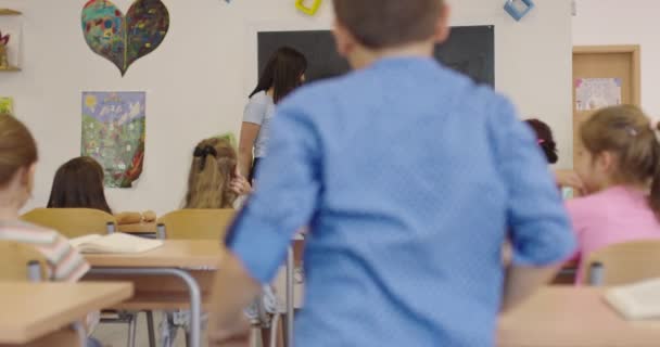 Die Lehrerin stellte ihren Schülern in der Grundschule eine Frage und der Junge hob die Hand, um die Antwort auf die Tafel zu schreiben. Lernprozess in der Schule. — Stockvideo