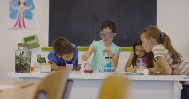 Aula de Ciencias de la Escuela Primaria: Profesor Entusiasta Explica Química a Diverso Grupo de Niños, Niño Pequeño Mezcla Químicos en Beakers. Niños aprenden con interés — Vídeo de stock