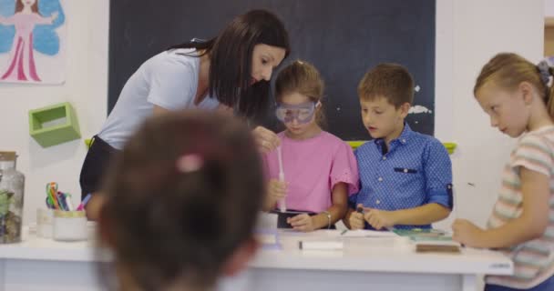 Grundskola Science Classroom: Entusiastisk lärare förklarar kemi för olika grupper av barn, små pojke blandar kemikalier i bägare. Barn lär sig med intresse — Stockvideo