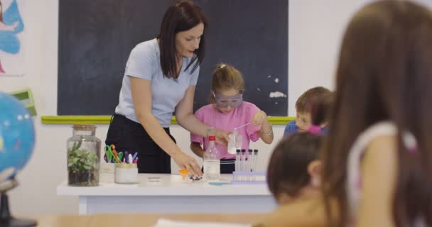 Általános Iskolai Tudomány Tanterem: Lelkes tanár elmagyarázza a kémiát a gyermekek különböző csoportjának, a kisfiú keveri a vegyi anyagokat a főzőpoharakban. A gyermekek érdeklődéssel tanulnak — Stock videók