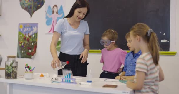 Sala de clasă de știință școlară elementară: Profesorul entuziast explică chimia unui grup divers de copii, băiețelul amestecă substanțele chimice în pahare. Copiii învață cu interes — Videoclip de stoc