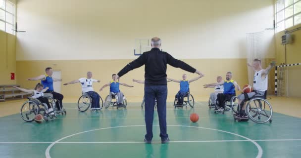 Селектор баскетбольной команды с ограниченными возможностями стоит перед игроками и показывает им упражнения на растяжку перед началом тренировки — стоковое видео