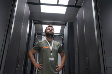 Erkek teknisyen ya da ağ yöneticisi portresi veri merkezi sunucu odasında kolları çaprazlanmış kahraman gibi duruyor. Yüksek kalite fotoğraf