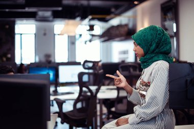 Çok ırklı girişimci Arap kadın takımı modern açık planlı ofis iç mimarisinde buluşmaya tesettüre girmiş, dizüstü bilgisayar ve bilgisayar üzerinde çalışıyor. Seçici odaklanma. Yüksek kalite