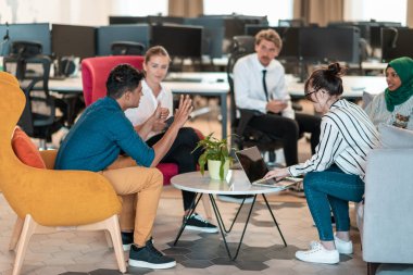 Modern ofis içinin rahatlama alanında beyin fırtınası yapan çok ırklı bir girişim ekibi dizüstü bilgisayar ve tablet bilgisayar üzerinde çalışıyor. Yüksek kaliteli fotoğraf.