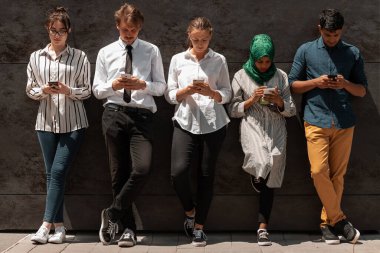 Dışarıdaki siyah duvarın önünde işten kahve molası verirken akıllı telefon kullanan çok ırklı bir iş adamı grubu. Yüksek kaliteli fotoğraf.