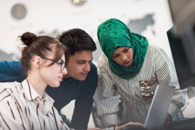 Çok ırklı girişimci Arap kadın takımı modern açık planlı ofis iç mimarisinde buluşmaya tesettüre girmiş, dizüstü bilgisayar ve bilgisayar üzerinde çalışıyor. Seçici odaklanma. Yüksek kalite