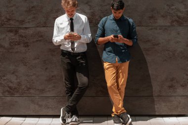 Geleneksel çok ırklı girişimci iş adamları. İçlerinden biri Hintli. İşten kaçarken dışarıda, gri duvarın önünde akıllı telefon kullanıyor. Yüksek kaliteli fotoğraf.
