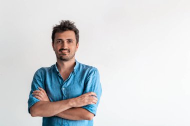 Resmi bir erkek portresi. Kendine güvenen başarılı bir iş adamı ya da yönetici beyaz bir arkaplan önünde duruyor, kollarını kavuşturup doğrudan kameraya bakıyor ve dostça gülümsüyor. Yüksek