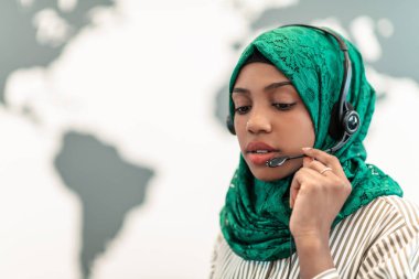 Yeşil başörtülü Afro Müslüman kadın müşteri temsilcisi telefon kulaklıklı iş kadını modern bir çağrı merkezinde müşteriye internet üzerinden yardım ve destek veriyor. Yüksek kaliteli fotoğraf.