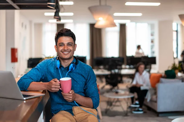 現代のオープンプランスタートアップオフィスのリラックスエリアでお茶を飲みながら ノートパソコンを使って仕事から休憩を取るカジュアルビジネスマン 高品質の写真 — ストック写真
