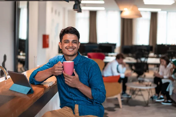 現代のオープンプランスタートアップオフィスのリラックスエリアでお茶を飲みながら ノートパソコンを使って仕事から休憩を取るカジュアルビジネスマン 高品質の写真 — ストック写真