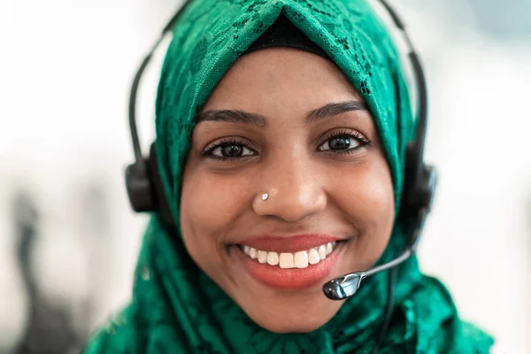 携帯電話のヘッドセットと緑のヒジャーブスカーフの顧客の代表的なビジネス女性とアフロイスラム教徒の女性は 現代のコールセンターで顧客とオンラインで支援し サポートしています 高品質の写真 — ストック写真