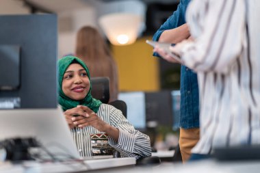 Çok ırklı girişimci Arap kadın takımı modern açık planlı ofis iç mimarisinde buluşmaya tesettüre girmiş, dizüstü bilgisayar ve bilgisayar üzerinde çalışıyor. Seçici odak 
