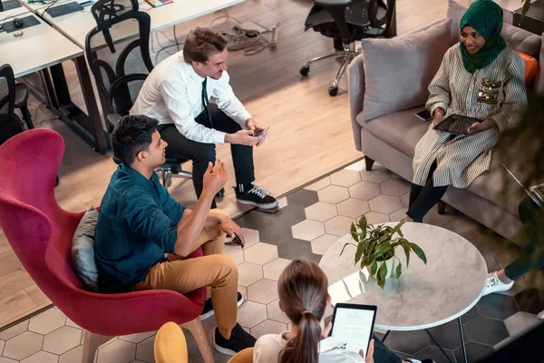 Equipe de negócios de inicialização multiétnica com brainstorming na área de relaxamento do interior do escritório moderno trabalhando em laptop e tablet — Fotografia de Stock