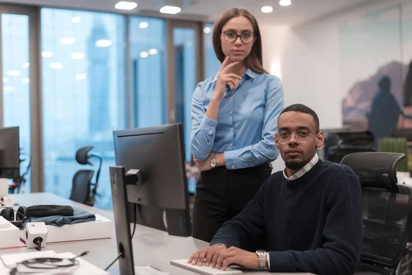 Young smiling woman explaining to serious African American coworker project strategy. Diverse startup coworkers students woman and man talking discussing working in modern office using computer. — Stock Photo, Image