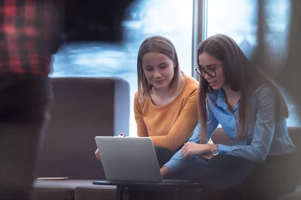 Dwie biznesmenki siedzą w nowoczesnej przestrzeni dla współpracowników w przerwie od pracy i relaksują się przy laptopie. Skupienie selektywne — Zdjęcie stockowe