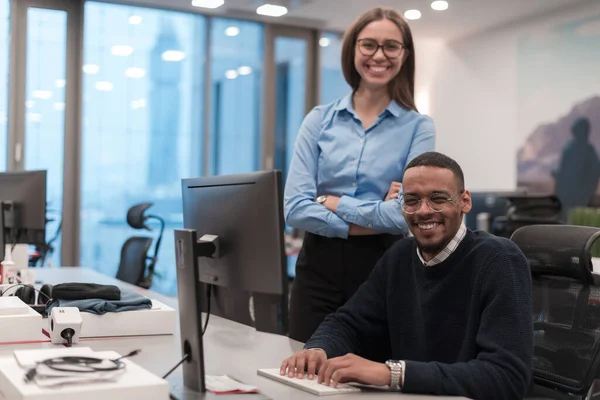 Jovem mulher sorrindo explicando a estratégia de projeto sério colega de trabalho afro-americano. Diversos colegas de startup estudantes mulher e homem falando discutir trabalhar no escritório moderno usando computador. Fotos De Bancos De Imagens