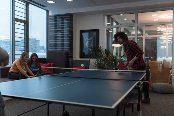 Zwei junge Start-up-Unternehmer spielen Ping-Pong-Tennis in modernen kreativen Büroräumen, im Hintergrund finden Treffen und Brainstorming statt — Stockfoto