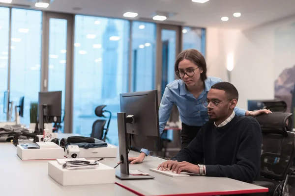 Junge lächelnde Frau erklärt ernsthaften afroamerikanischen Mitarbeitern die Projektstrategie. Diverse Start-up-Mitarbeiter Studenten und Männer diskutieren über das Arbeiten im modernen Büro mit dem Computer. Stockfoto