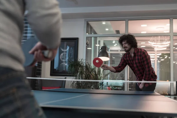 两个年轻的创业者在现代创意办公空间打乒乓球，人们聚集在一起，在幕后集思广益 — 图库照片