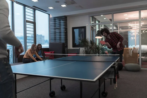 两个年轻的创业者在现代创意办公空间打乒乓球，人们聚集在一起，在幕后集思广益 — 图库照片