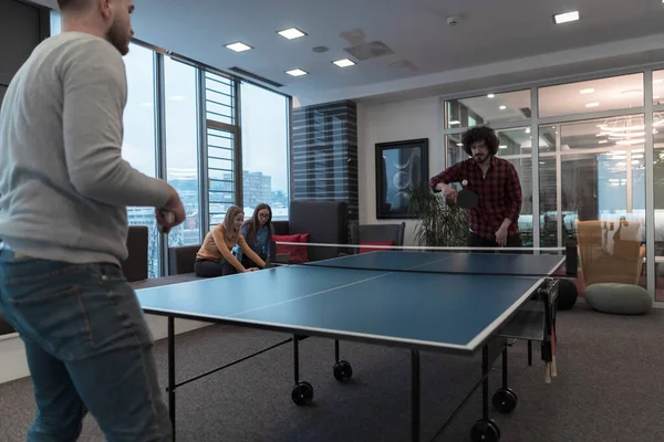 Két fiatal start up üzletember ping-pong teniszezik a modern kreatív irodahelyiségben emberek csoportjának találkozója és ötletelése a háttérben — Stock Fotó