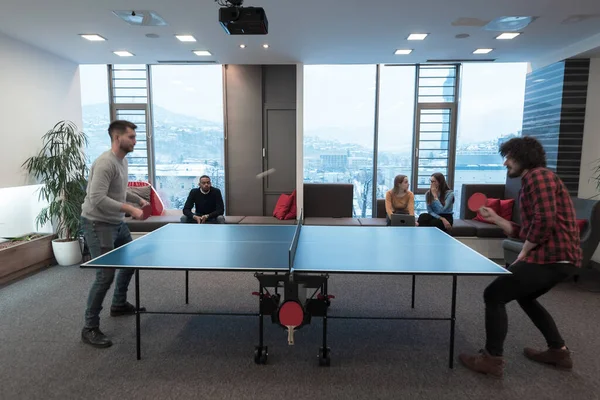 Dos jóvenes hombres de negocios de nueva creación jugando ping pong tenis en el moderno espacio de oficina creativa grupo de personas tienen reunión y lluvia de ideas en segundo plano —  Fotos de Stock