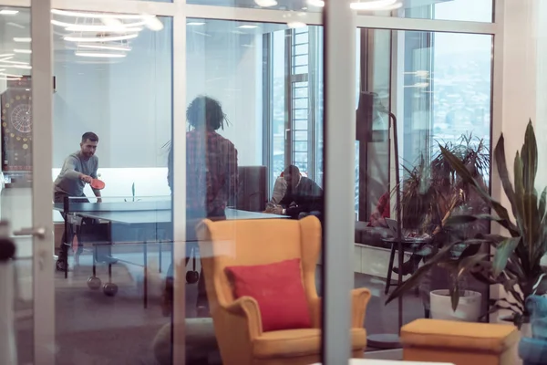Zwei junge Start-up-Unternehmer spielen Ping-Pong-Tennis in modernen kreativen Büroräumen, im Hintergrund finden Treffen und Brainstorming statt — Stockfoto