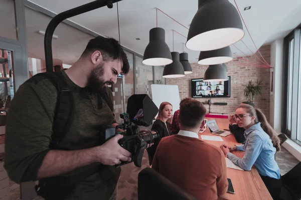 Nos bastidores. Cameraman gravando um grupo de jovens empresários multiétnicos que trabalham e se comunicam juntos em um escritório criativo. Foco seletivo — Fotografia de Stock