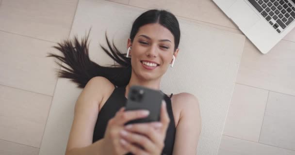 Hermosa chica usando Smartphone después del entrenamiento de fitness en casa. Determinado tamaño más mujer usando Fitness Tracker, Aplicación de ejercicios de yoga, Navegar artículos de salud en línea, Publicar en Internet — Vídeos de Stock