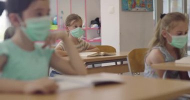 Sınıftaki maskeli çocuklar sınıfta oturur ve öğretmenlerini dinlerler. Okulda salgın sırasında alınan dersler.