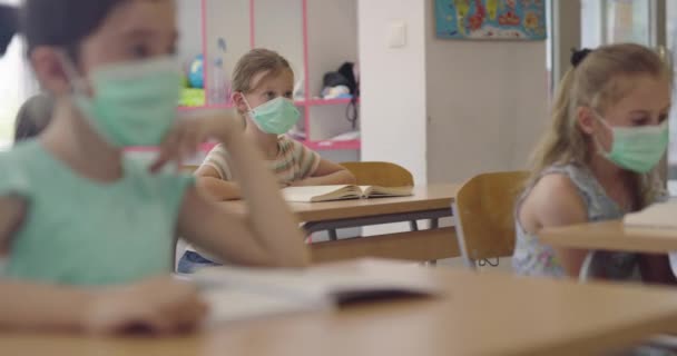 Děti ve škole v maskách sedí ve třídě a poslouchají učitele. Lekce během pandemie ve škole. — Stock video