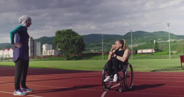 Žena s postižením zahřívání na invalidním vozíku na atletické tréninkové dráze s muslimskou ženou na sobě hidžáb sportovní oblečení — Stock video