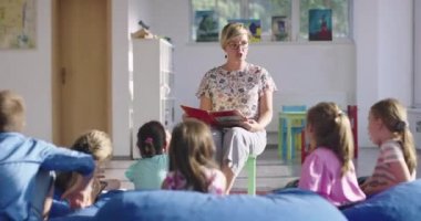 Öğretmen ilkokuldaki çocuklara kitap okuyor.
