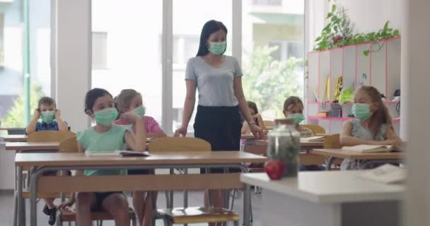 在学校里，女教师戴着面具，在学校的教室里教孩子们。Covid19 Coronavirus大流行病期间重返校园健康安全教育. — 图库视频影像