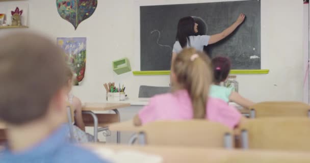 Leerproces op school, vrouwelijke leraar schrijft met krijt op het schoolbord. — Stockvideo