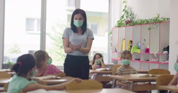 Wielorasowa grupa dzieci w maskach pracujących w klasie, piszących i słuchających wyjaśnień nauczyciela w klasie — Wideo stockowe