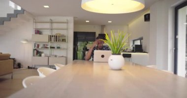 Afro-Amerikalı iş adamı akıllı telefon ve laptop kullanarak online konferans videosu çekiyor. Erkek çağrı merkezi ajanı, yönetici modern bir ev ofisinde web kamerası toplantısı yapıyor.