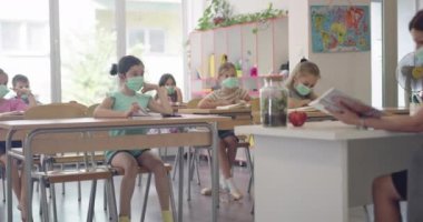 Sınıftaki maskeli çocuklar sınıfta oturur ve öğretmenlerini dinlerler. Okulda salgın sırasında alınan dersler.