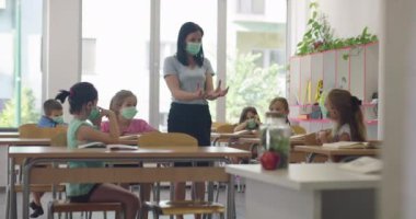 Sınıfta çalışan, sınıfta çalışan, öğretmenlerin açıklamalarını dinleyen ve yazan çok ırklı maskeler takan bir grup çocuk.