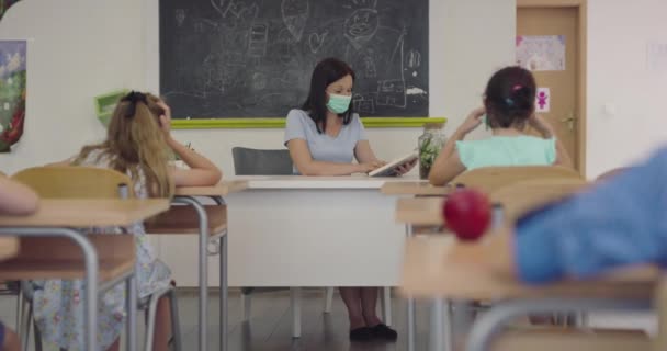 Kvindelig lærer iført ansigtsmaske i skolen, undervise børn i skolen klasseværelse. Uddannelse tilbage til skolen sundhed sikkerhed under Covid19 Coronavirus pandemi. – Stock-video