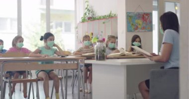Sınıftaki maskeli çocuklar sınıfta oturur ve öğretmenlerini dinlerler. Okulda salgın sırasında alınan dersler.