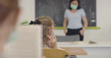 Öğretmen çocuk öğrenciyle yüzüne maske takması için konuşuyor. Okulda salgın sırasında alınan dersler.