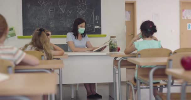 Nauczycielka w masce w szkole, ucząca dzieci w klasie. Edukacja z powrotem do bezpieczeństwa szkolnego podczas pandemii Covid19. — Wideo stockowe
