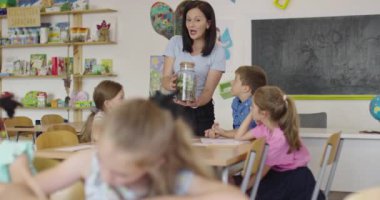 İlkokulda biyoloji sınıfında çocuklu bir bayan öğretmen biyoloji ya da sürdürülebilir bitkilerle ilgili botanik bilimsel deney yapıyor. Bitkileri bir bardakta öğrenmek.