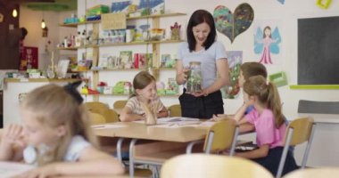 İlkokulda biyoloji sınıfında çocuklu bir bayan öğretmen biyoloji ya da sürdürülebilir bitkilerle ilgili botanik bilimsel deney yapıyor. Bitkileri bir bardakta öğrenmek.