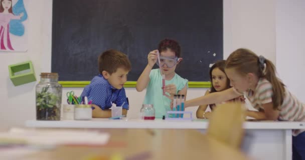 Sala de clasă de știință școlară elementară: Profesorul entuziast explică chimia unui grup divers de copii, băiețelul amestecă substanțele chimice în pahare. Copiii învață cu interes — Videoclip de stoc